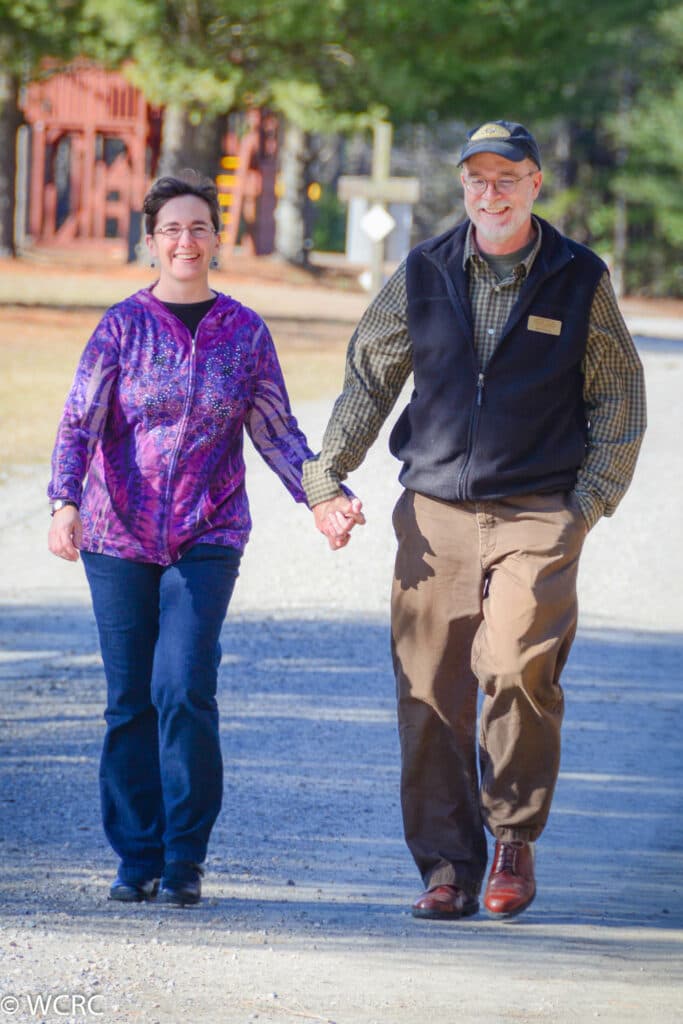 A Married Couple Walking And Holding Hands Outside Of Williamsburg Church Retreat Center In Virginia.