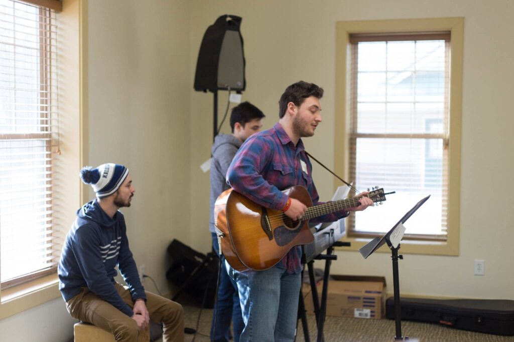 Winter Youth Retreat 2024 8 Men Playing Musical Instruments While Singing Together In A Retreat Center Building At Wcrc During A Winter Retreat Event.