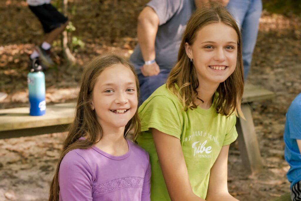Two Girls Smiling While Sitting On A Wooden Bench Together At Wcrc'S Family Harvest Festival